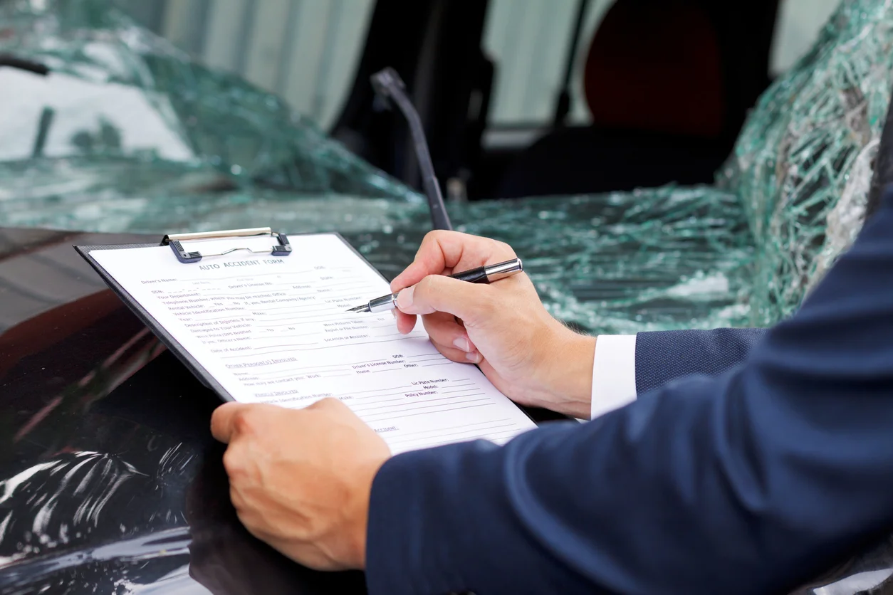 An over-the-shoulder shot of a man in a business suit signing documents while next to a car accident representing the car accident attorneys at Trident Law HQ