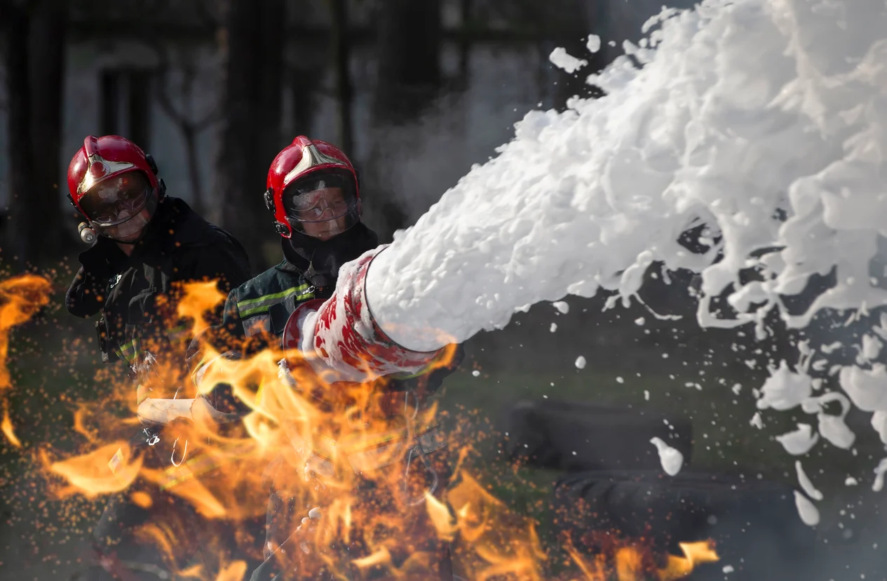 A firefighter spraying thick foam to put out a fire which showcases hazardous chemical exposure linked to firefighting foam claims litigated by Trident Law HQ