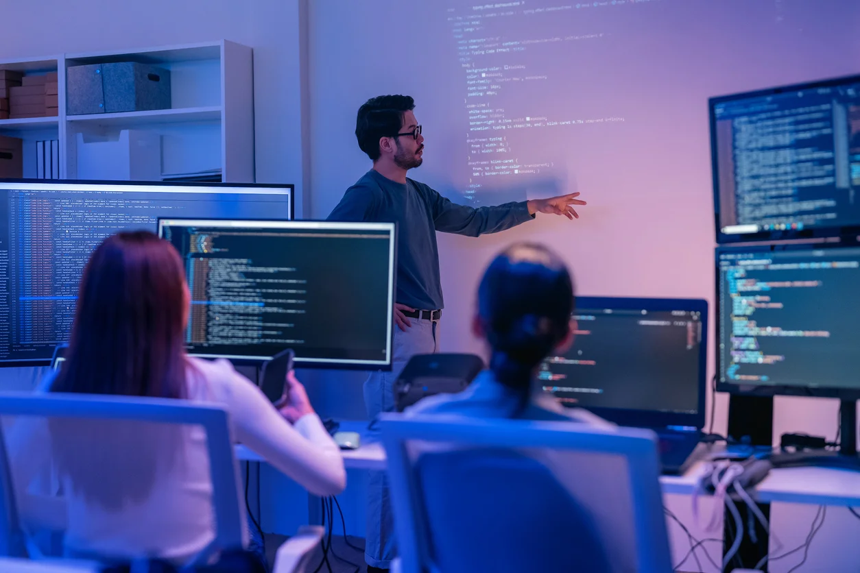 A group of software developers, one standing next to a screen and two others watching from their desks representing labor rights, wage disputes, and labor law cases supported by Trident Law HQ