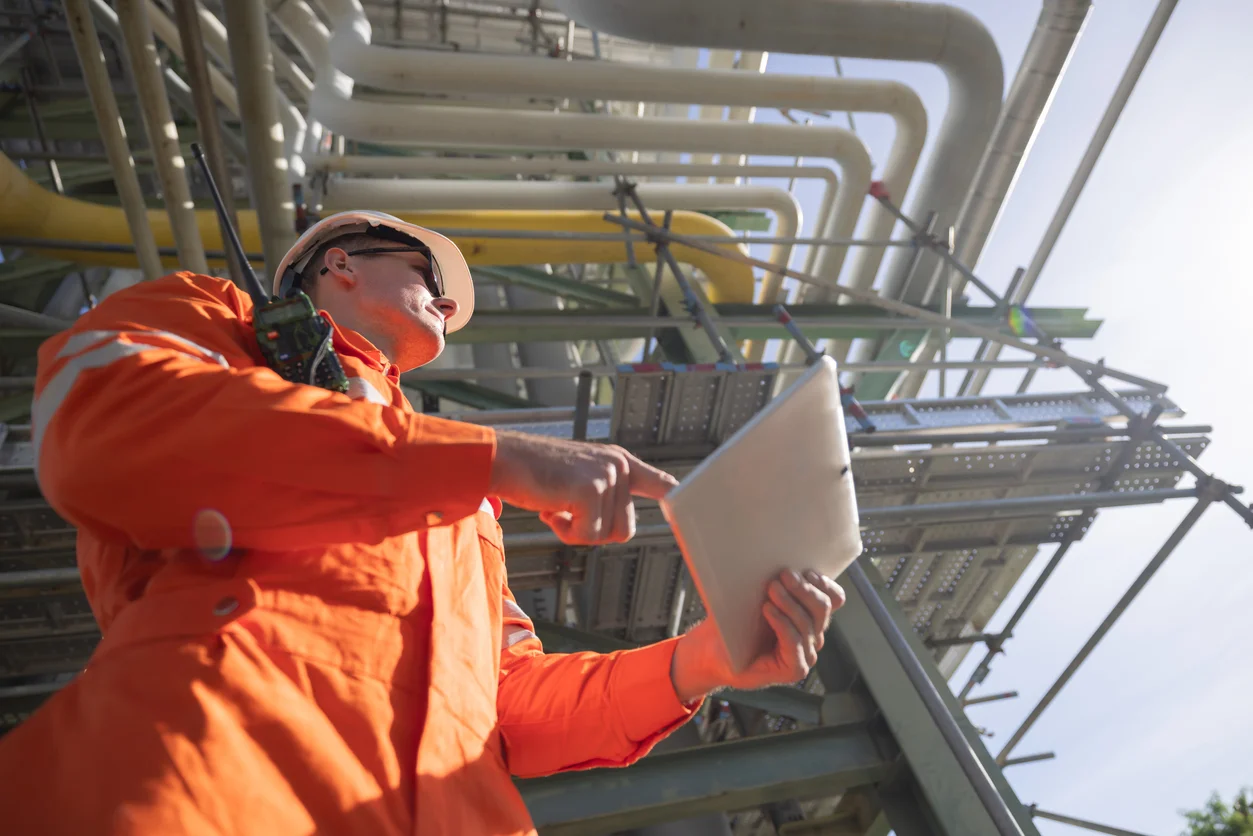 This low-angle shot shows a male worker in an orange jumpsuit surveying an oil rig, some of which can be seen above capturing hazardous offshore conditions and oil rig accident claims handled at Trident Law HQ