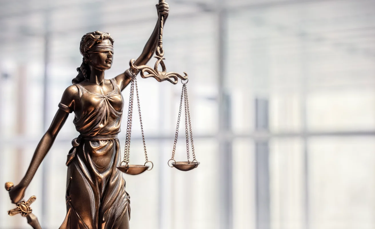 An close-up image of a golden scales of justice figure against an office background to represent Trident Law HQ