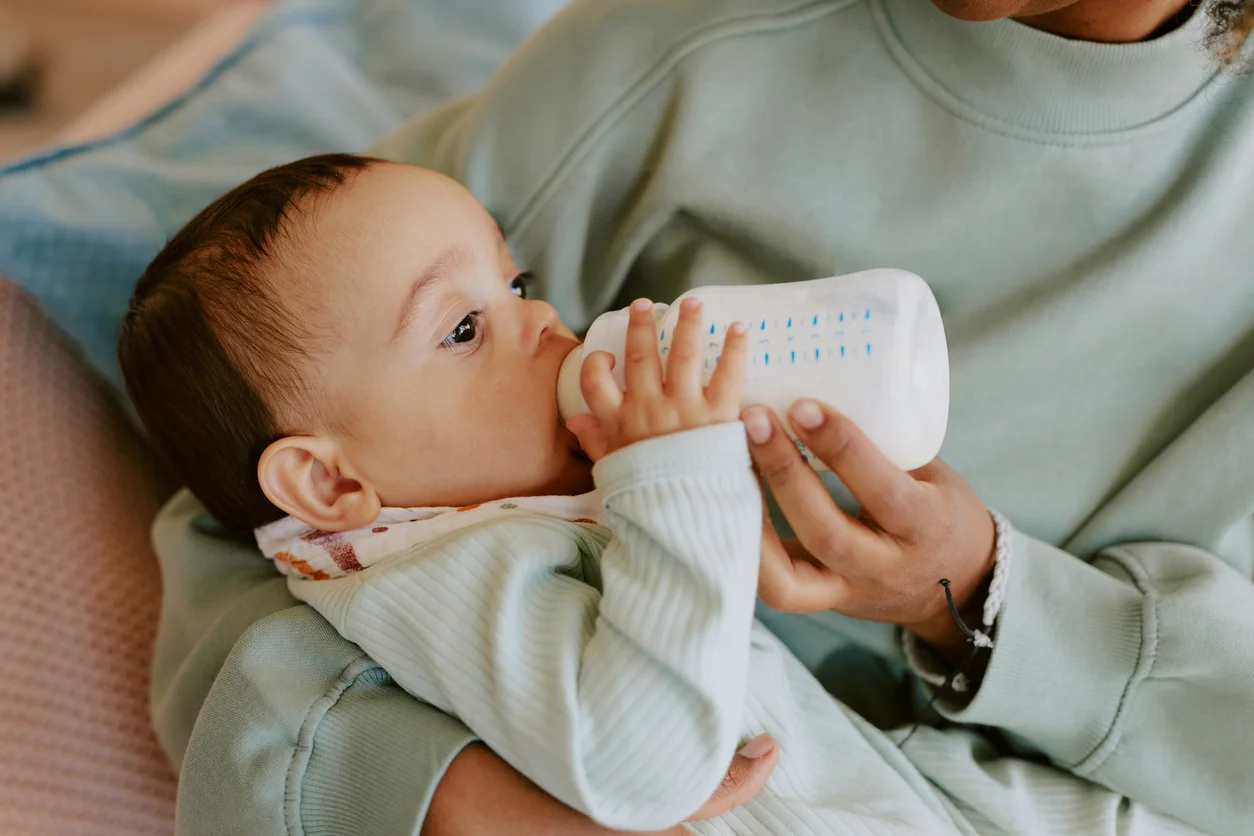 A baby drinking formula out of a bottle while being held by its mother representing infant injury risks and baby formula contamination lawsuits handled at Trident Law HQ