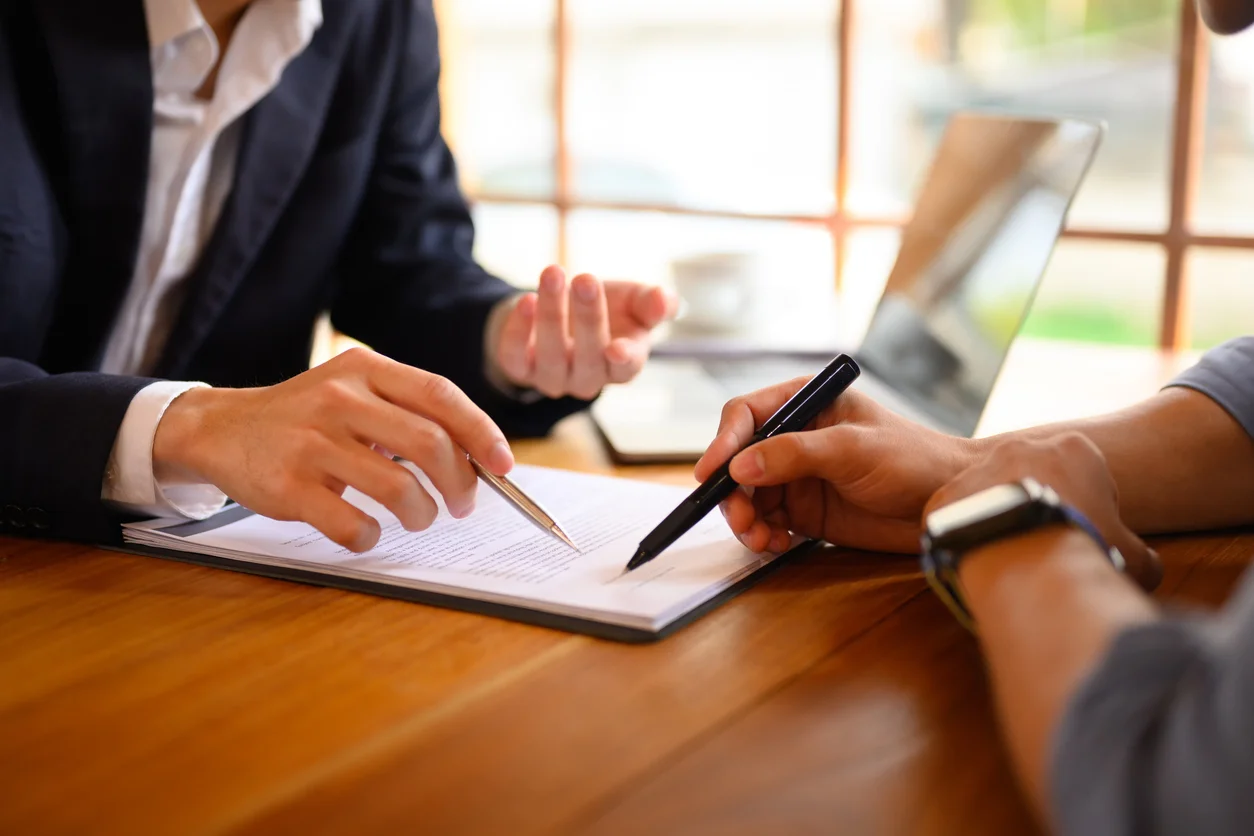 A close-up of a pair of hands pointing out something on a contract  while the other holds a black pen symbolizing delayed or denied coverage related to bad faith insurance disputes managed by Trident Law HQ