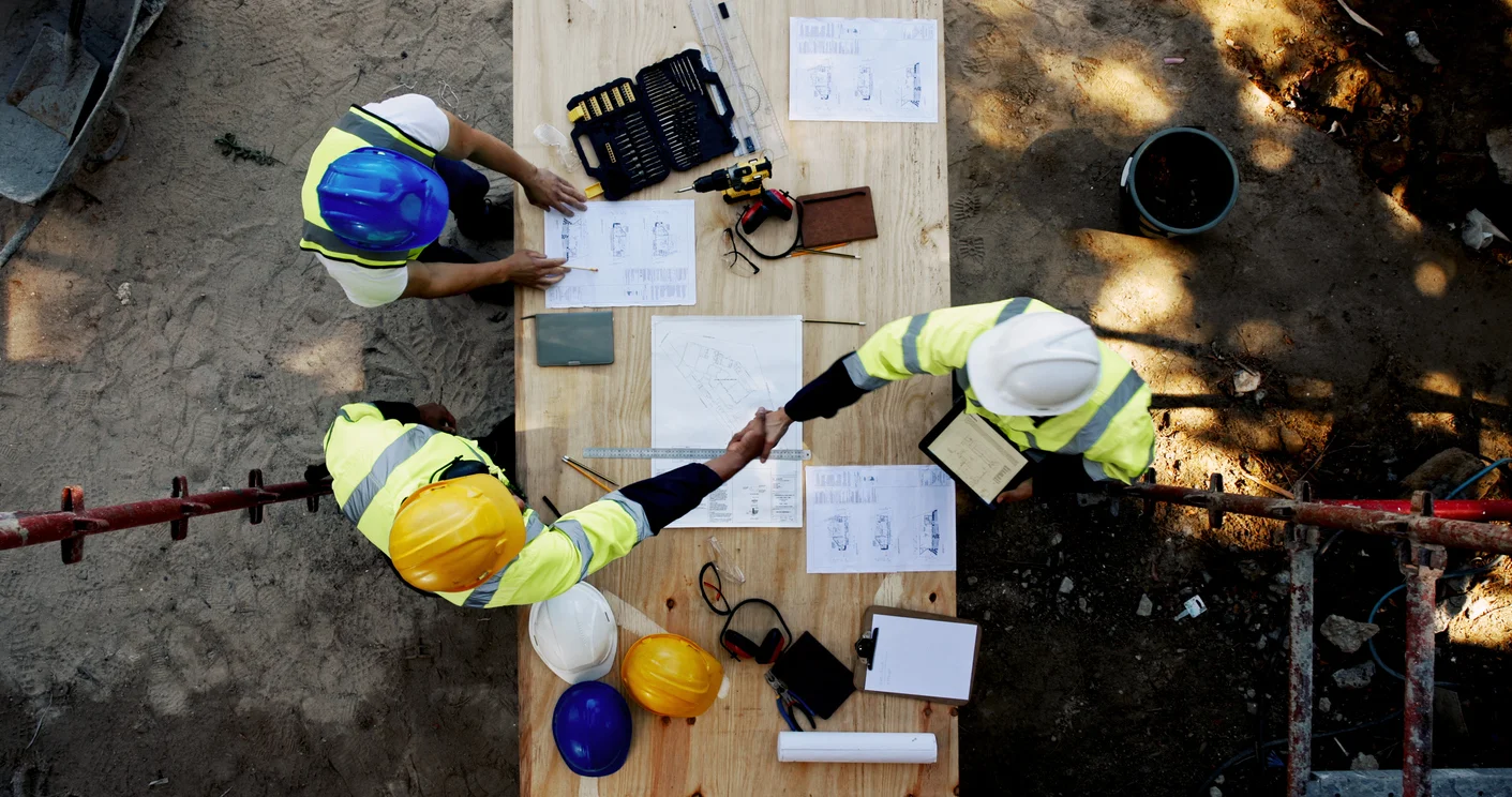 An aerial view of a group of workers wearing construction hats pouring over blueprints symbolizing faulty construction, structural defects, and related litigation handled by Trident Law HQ