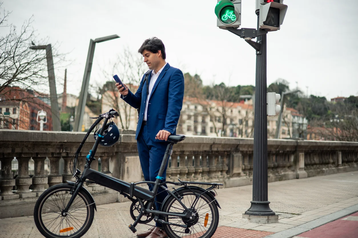 An image of a man in a suit looking down at his electronic bicycle next to a traffic light illustrating electric bike collision and e-bike injury claims handled at Trident Law HQ