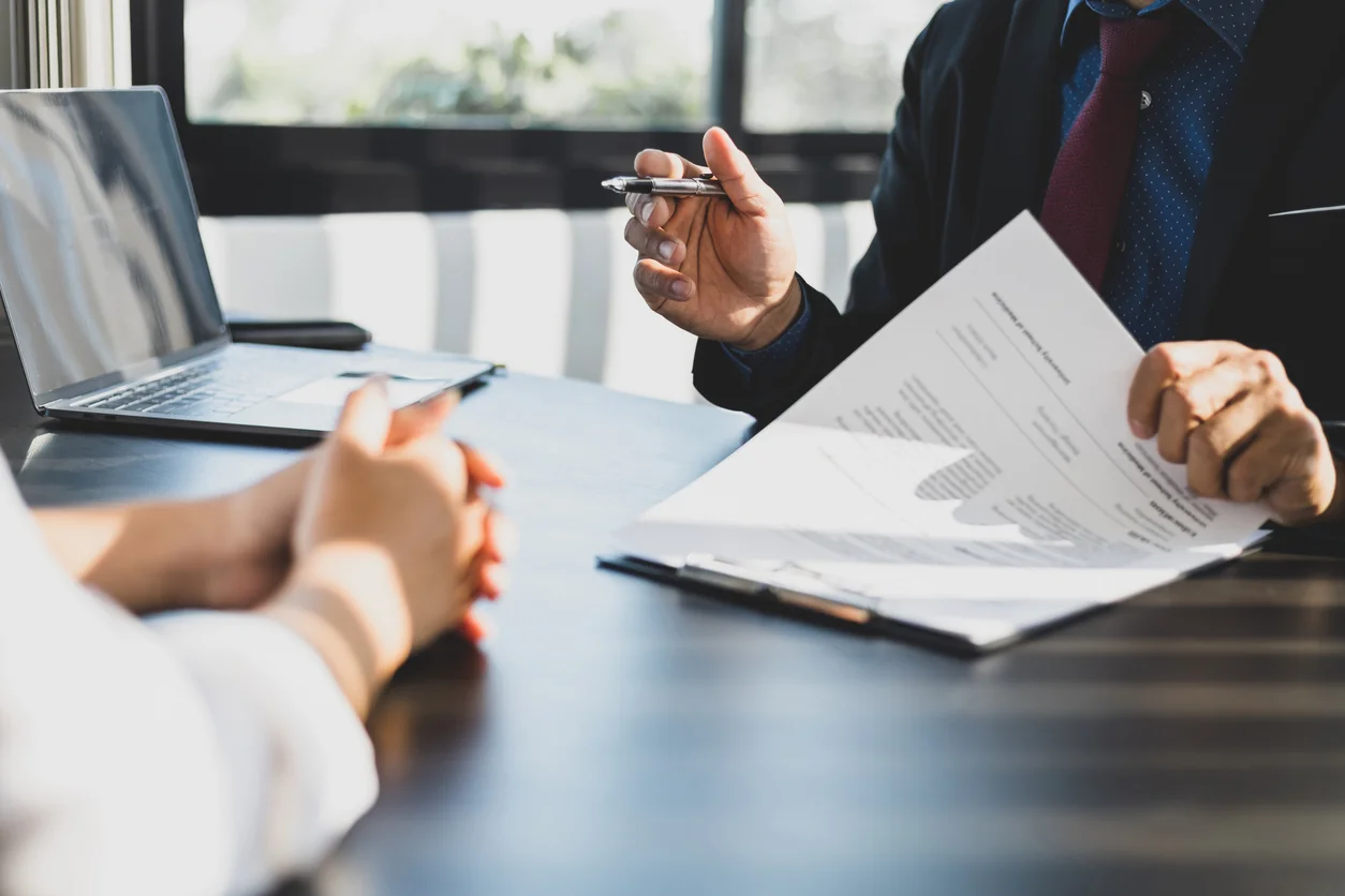 An image of a pair of hands holding a pen and another pair of hands holding a pen and gesturing to a contract representing property damage disputes and homeowners insurance claims handled by Trident Law HQ