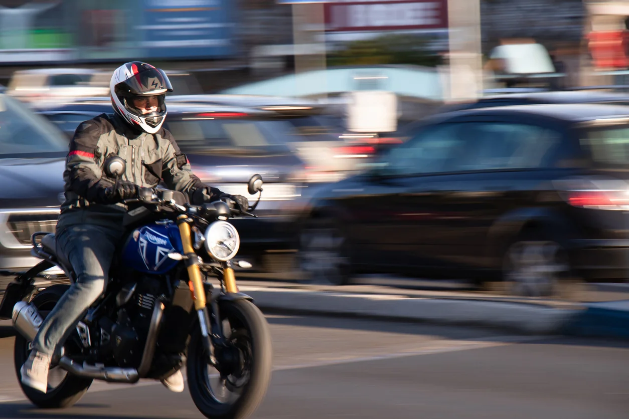 A man wearing a helmet driving a black motorcycle against a blurry background representing motorcycle crash injury claims advocated by Trident Law HQ