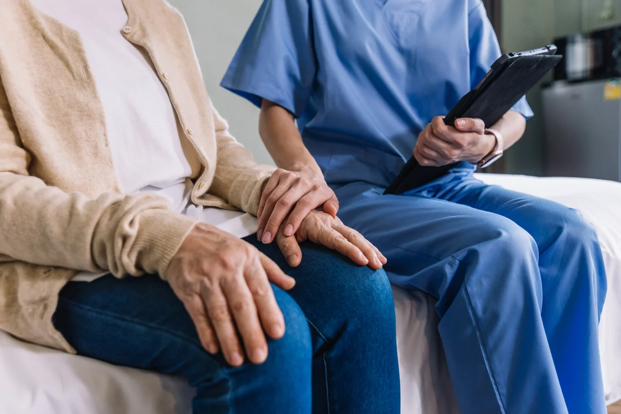 Trident Law HQ advocates for vulnerable seniors, shown here by an image of caregiver dressed in blue holding a tablet with one hand and holding the hand of a senior with the other