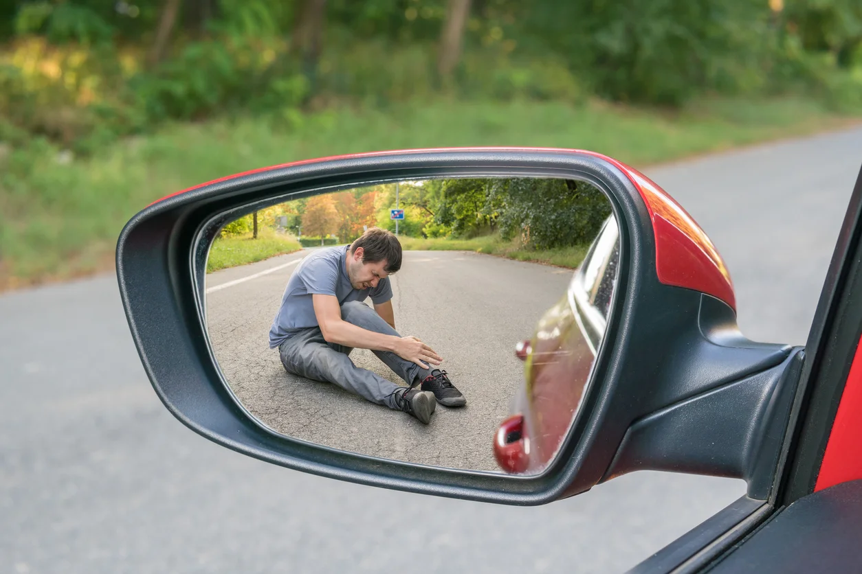 A rearview mirror shot of a man on the pavement clutching his hurt ankle symbolizing pedestrian accident injuries and legal action managed by Trident Law HQ
